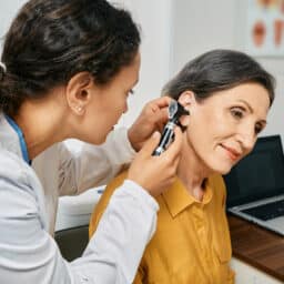 Hearing exam for elderly citizen people. Otolaryngologist doctor checking mature woman's ear using otoscope or auriscope at medical clinic