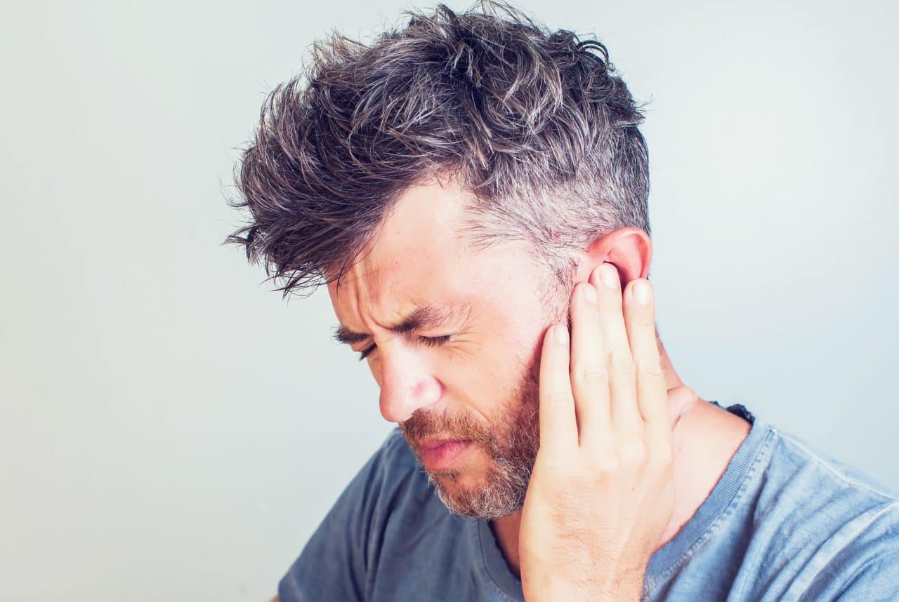 Man with tinnitus pressing his ear.