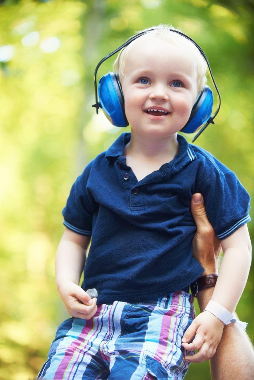 Cute little boy lifted up by his father while wearing noise-canceling headphones