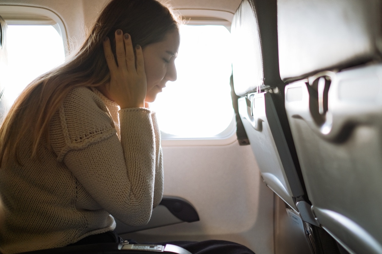 Woman on an airplane covering her ears.